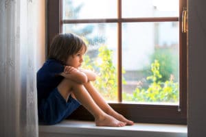 A young boy sitting on a window sill, gazing out after school.
