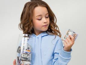 A motivated little girl is holding a jar of money.