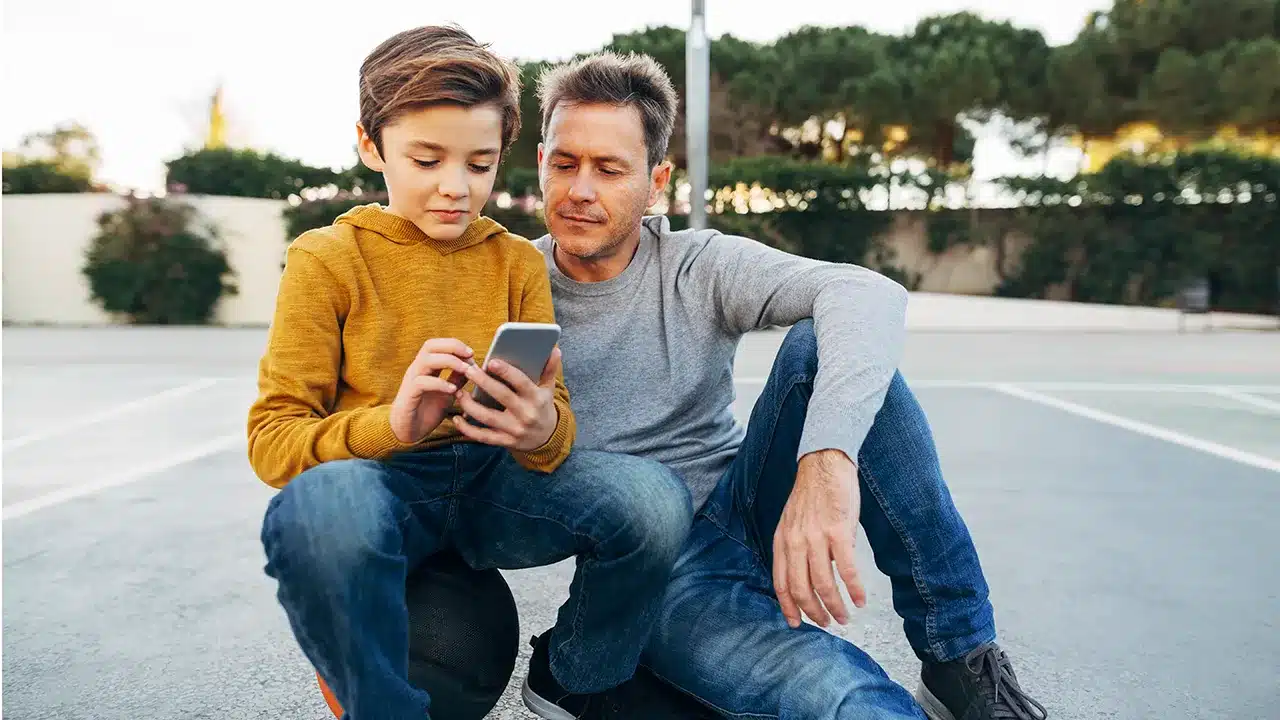 A father and son, engrossed in the BusyKid app on their cell phone.