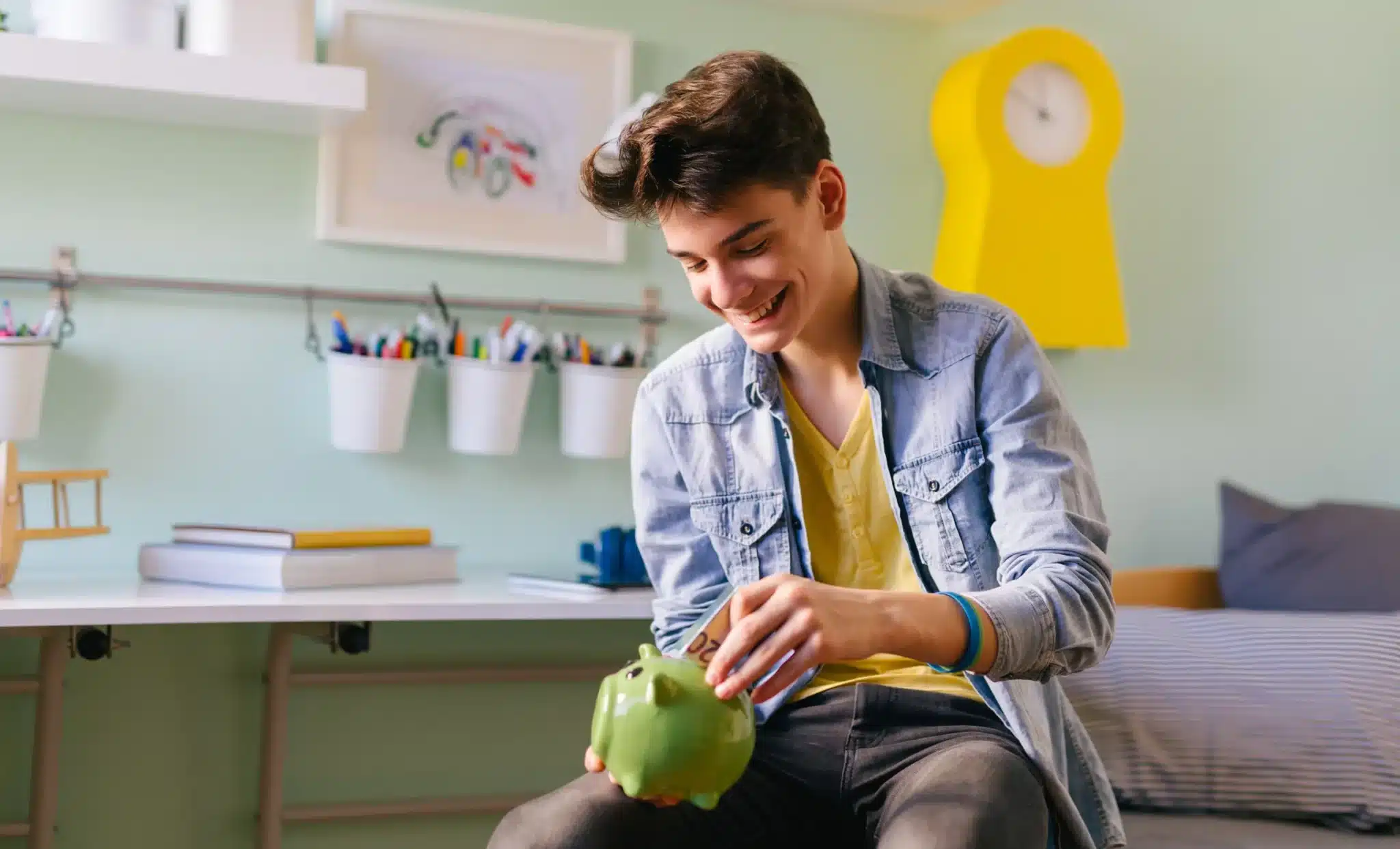 A teen sitting on a bed, diligently saving money in a piggy bank.